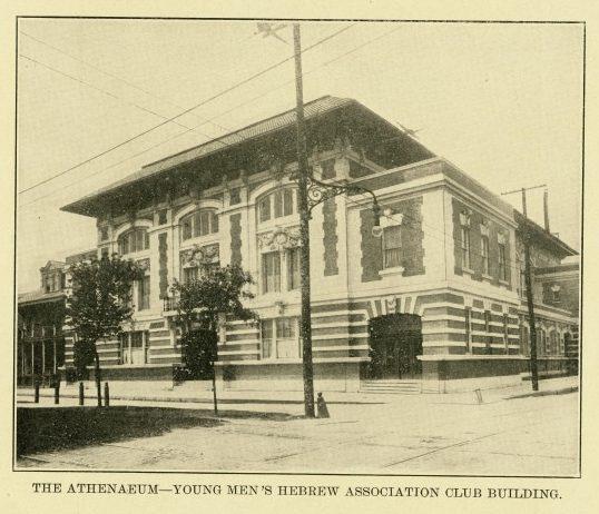 Vintage photo of the Athenaeum—Young Mens Hebrew Association Club Building. A grand, ornate structure with arched windows and decorative details on a corner lot. Streets are empty, and a streetlamp is visible in the foreground.