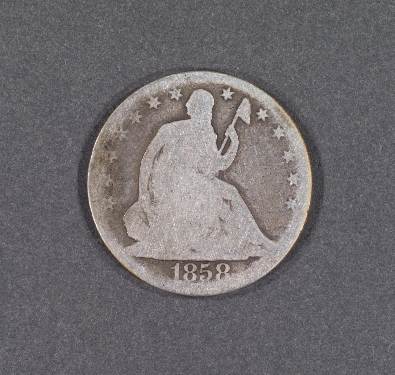 A 1858 silver coin featuring a seated figure holding a staff, surrounded by stars along the edge.