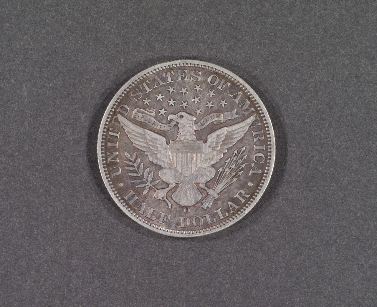 An old American half dollar coin featuring an eagle with outstretched wings, a shield on its chest, and a banner reading E Pluribus Unum. The coin is surrounded by the text United States of America Half Dollar and stars.
