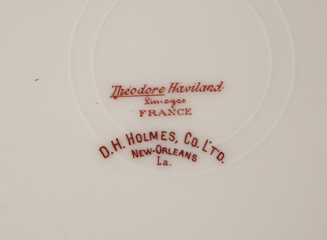 A close-up of a ceramic backstamp featuring the text Théodore Haviland Limoges France in red. Below it, D.H. Holmes, Co. Ltd. New Orleans La. is printed, also in red, on a white background.