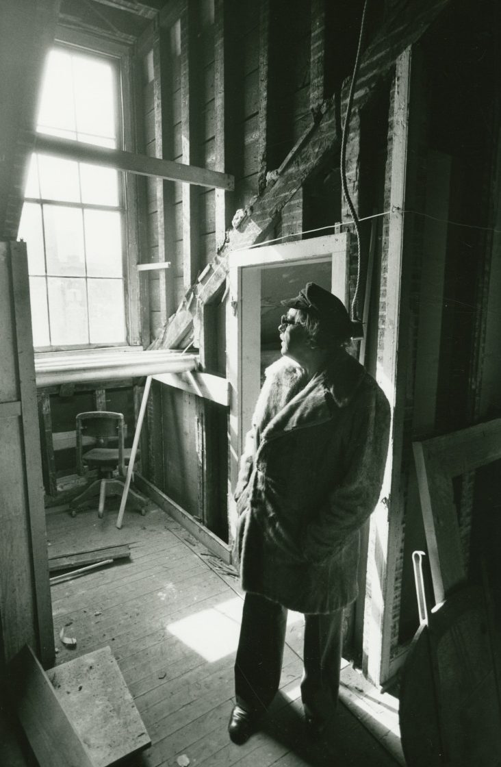 View of Thomas Lanier Williams standing in the attic of the building located at 722 Toulouse Street in the Vieux Carré. He wears a seaman's cap, sunglasses, and a fur coat.