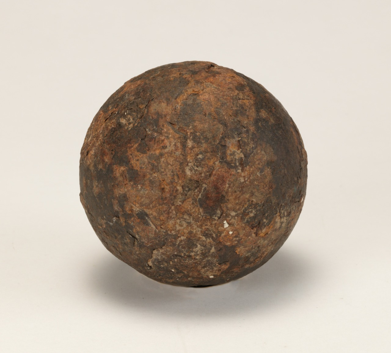 A heavily rusted metal cannonball with a rough, textured surface, set against a plain white background.