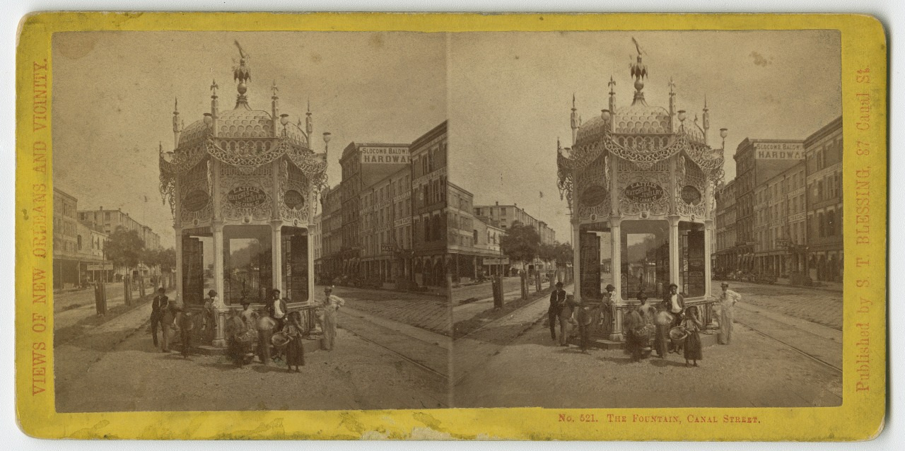 A vintage stereoscopic image of a decorative fountain in Cane Street, New Orleans. It features intricate designs and is surrounded by several men in 19th-century attire. Buildings line the street in the background.