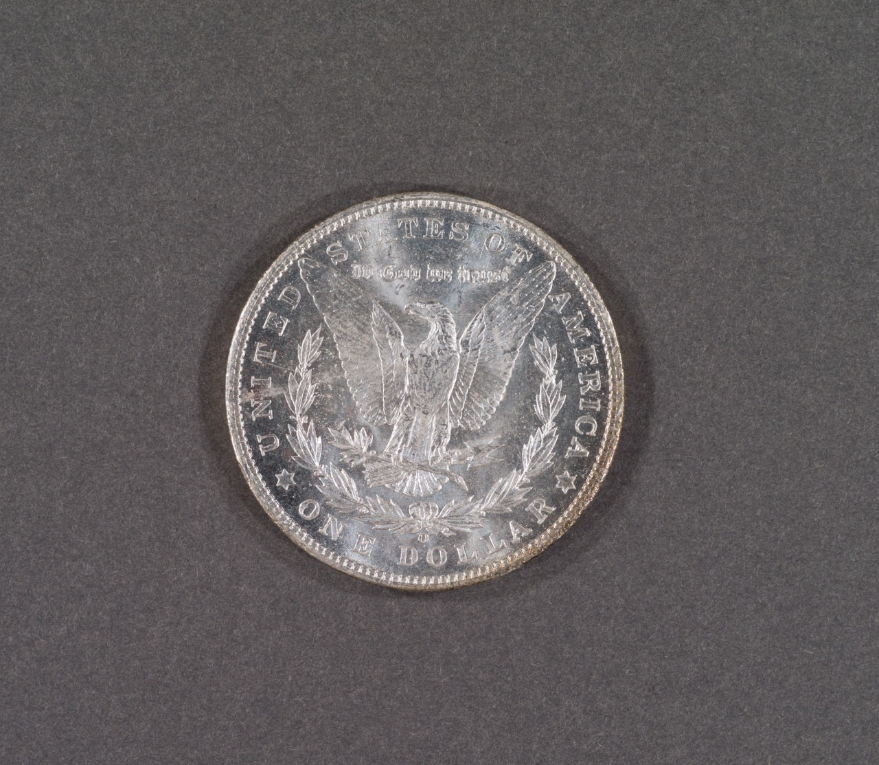 Image of a U.S. silver dollar coin featuring an eagle with outstretched wings surrounded by the words United States of America and One Dollar. The coins intricate details are captured against a plain, dark background.