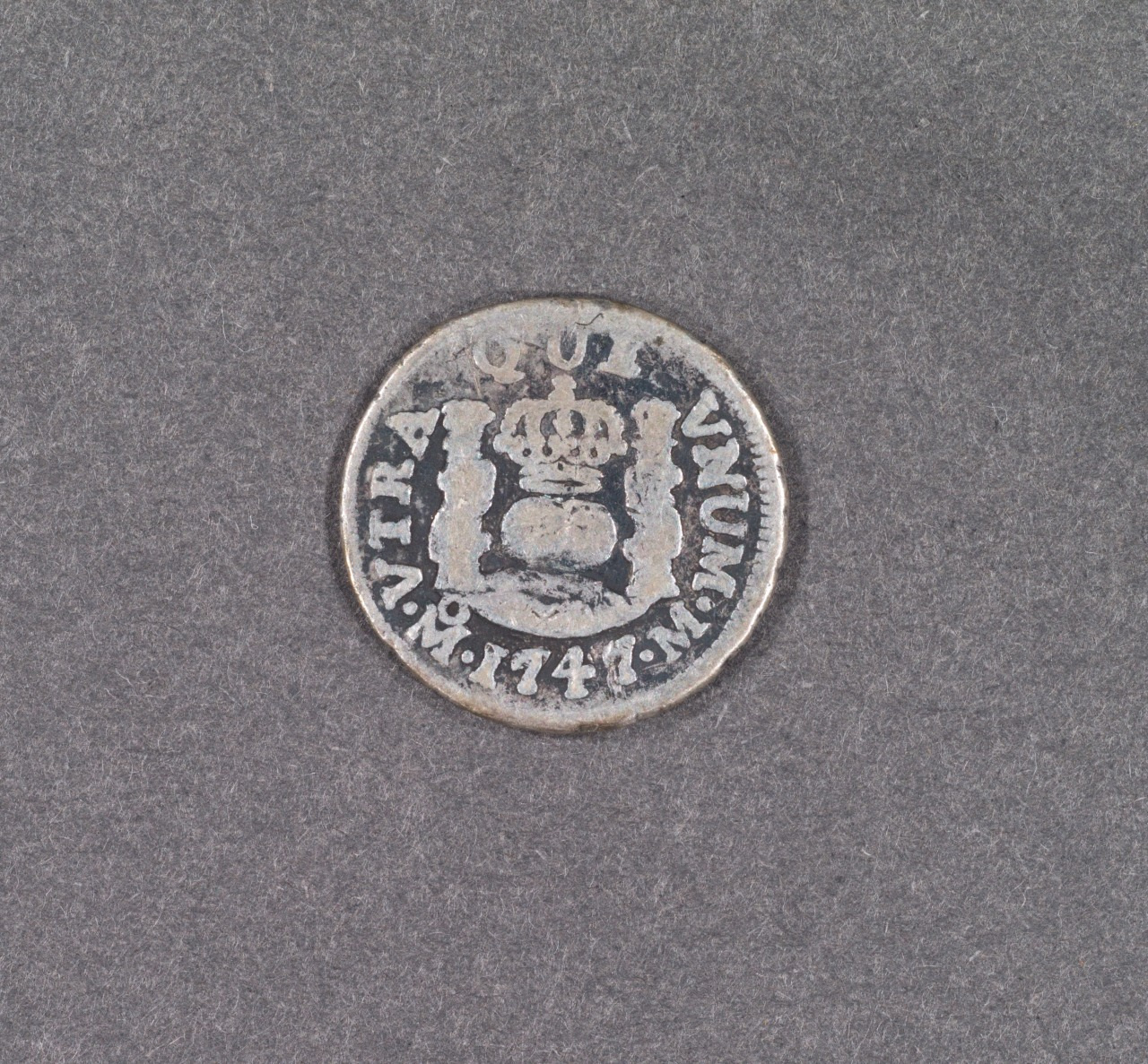 A vintage coin with inscriptions and symbols, including a crown and fortress, dated 1744. The background is plain gray.