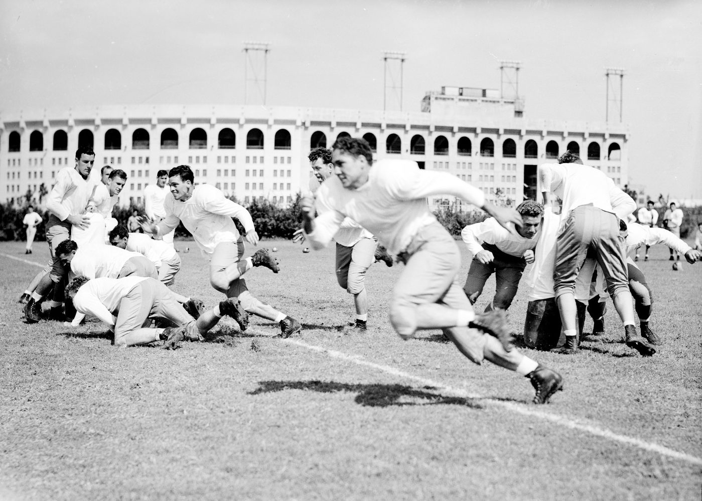 A black and white photo of football players tackling each other and running.