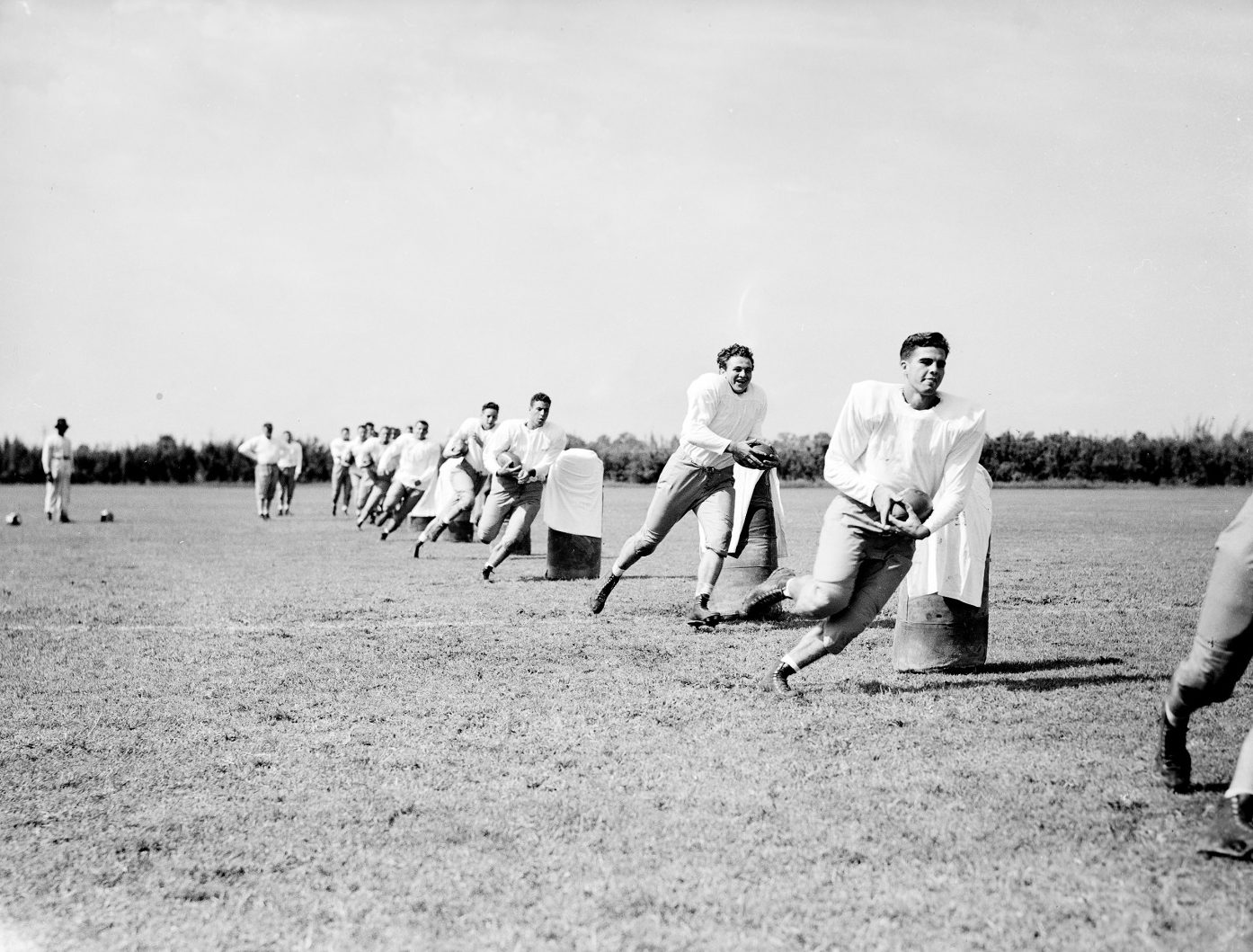 A group of football players run through a row of blocking dummies on a field outside of Tiger Stadium on the campus of Louisiana State University.