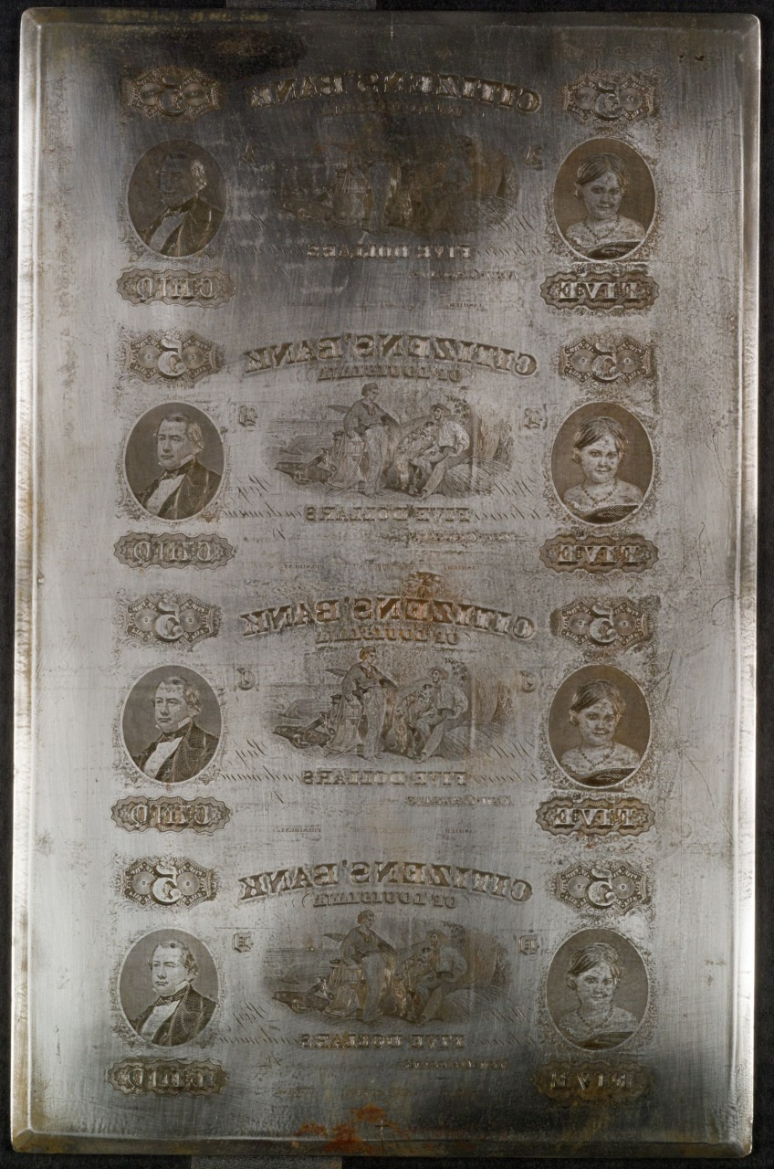An antique printing plate featuring engravings of banknotes. It displays intricate designs, portraits, and bank-related text. The metal surface shows signs of age and wear, adding a historical charm to the piece.