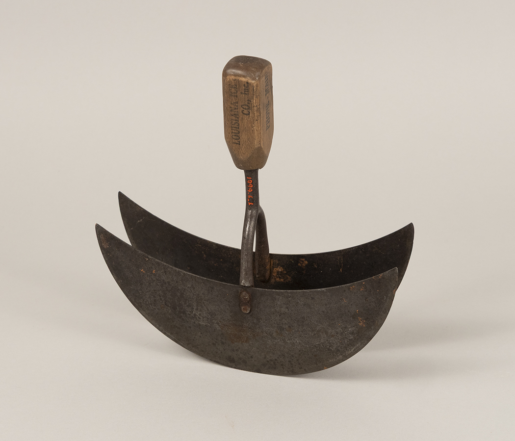 Photograph of an ice chopper for breaking down ice block deliveries in the kitchen. It is composed of two crescent-shaped blades with a wooden handle.