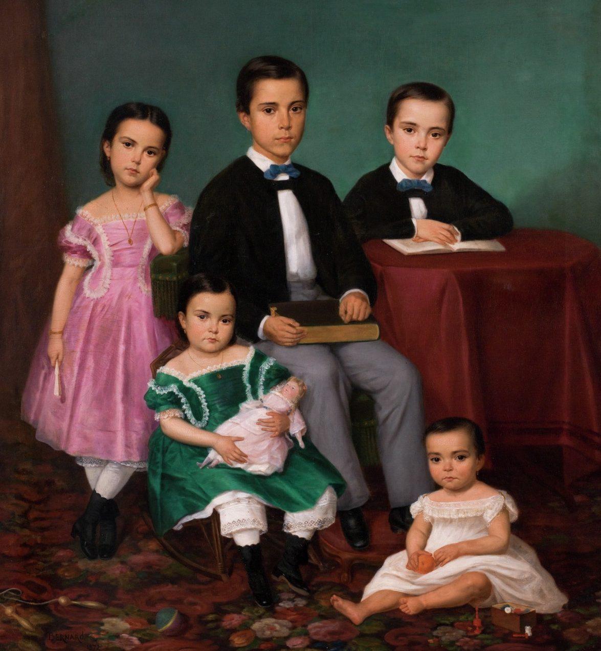 A classic portrait of five children: two boys in the center wearing suits and bow ties, two girls in colorful dresses standing beside them, and a toddler in a white gown sitting on the floor with an orange ball. A book rests on the boys lap.