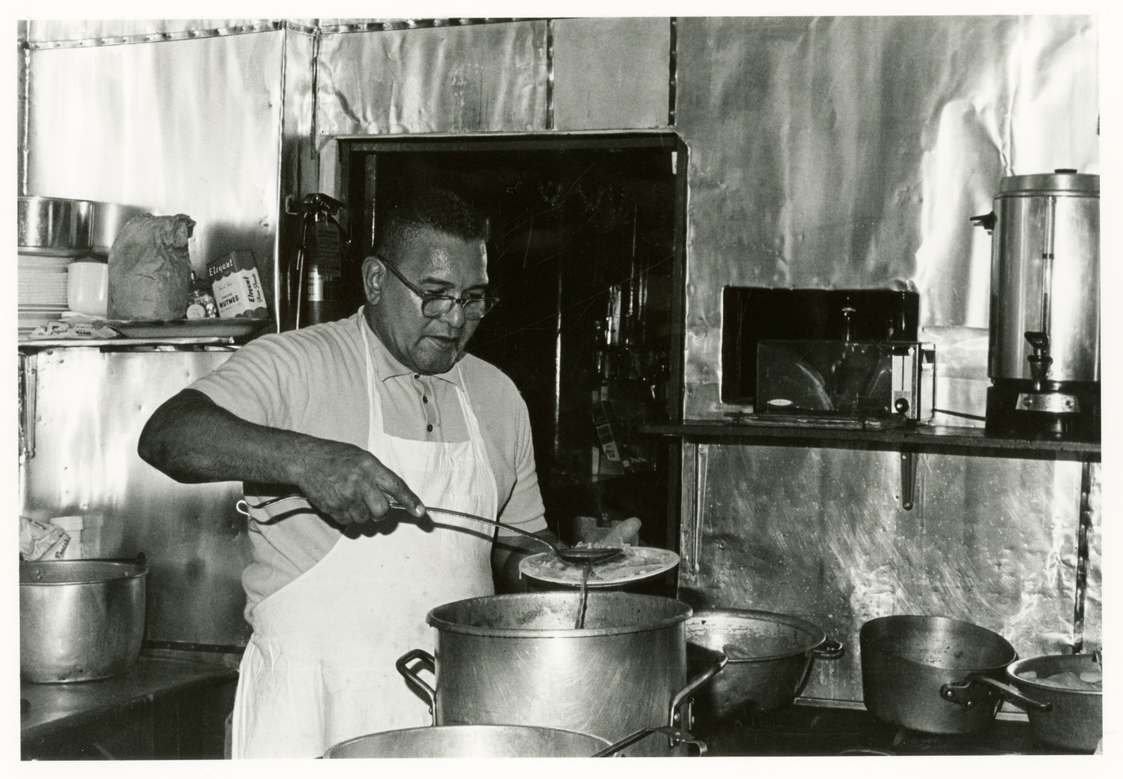 View of Buster Holmes in a kitchen ladling food onto a plate.