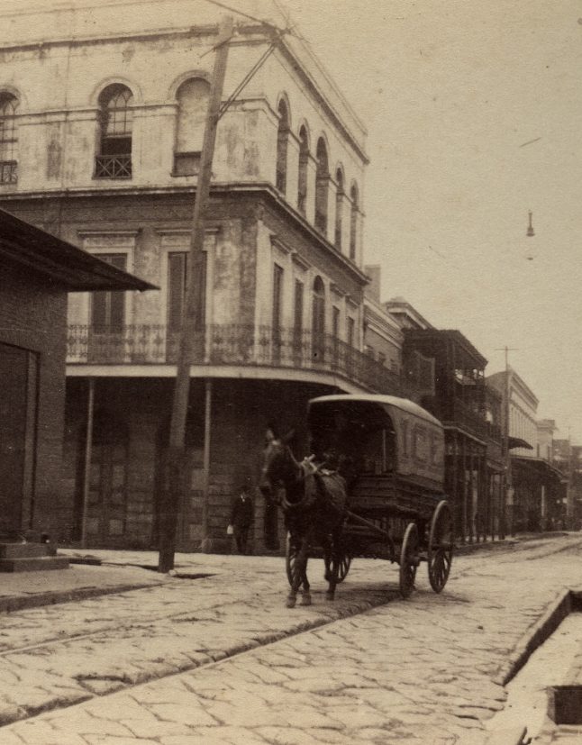 A horse-drawn carriage with "ICE" written on the side moving through the French Quarter.