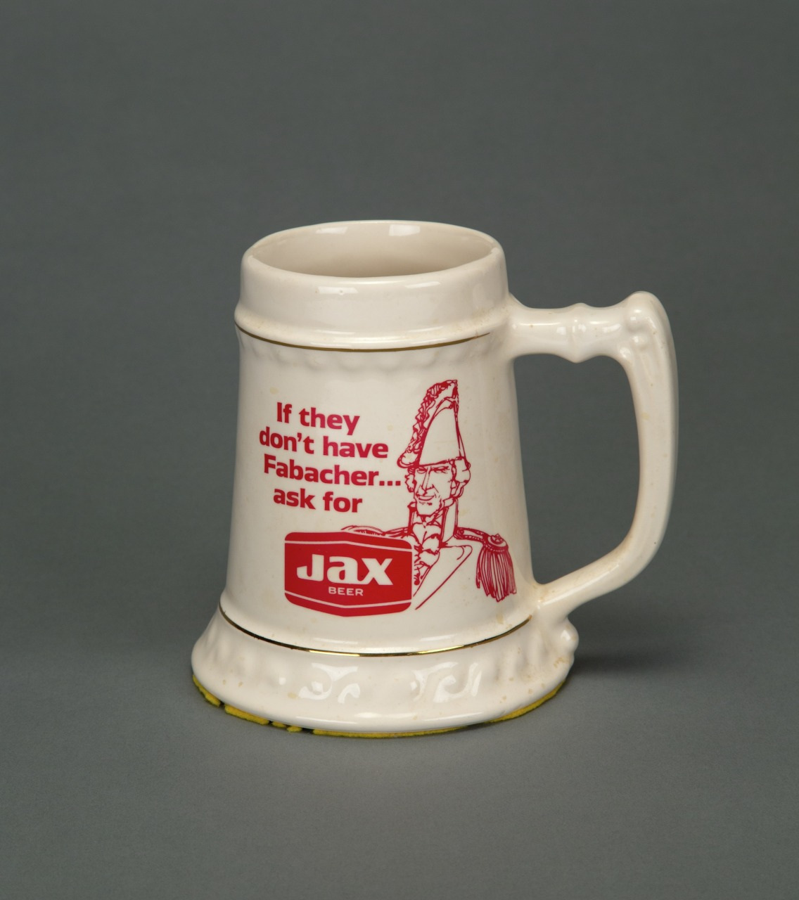A white ceramic beer mug with a printed red text and illustration. The text reads, If they dont have Fabacher... ask for JAX BEER, next to a drawing of a person in a historical uniform.