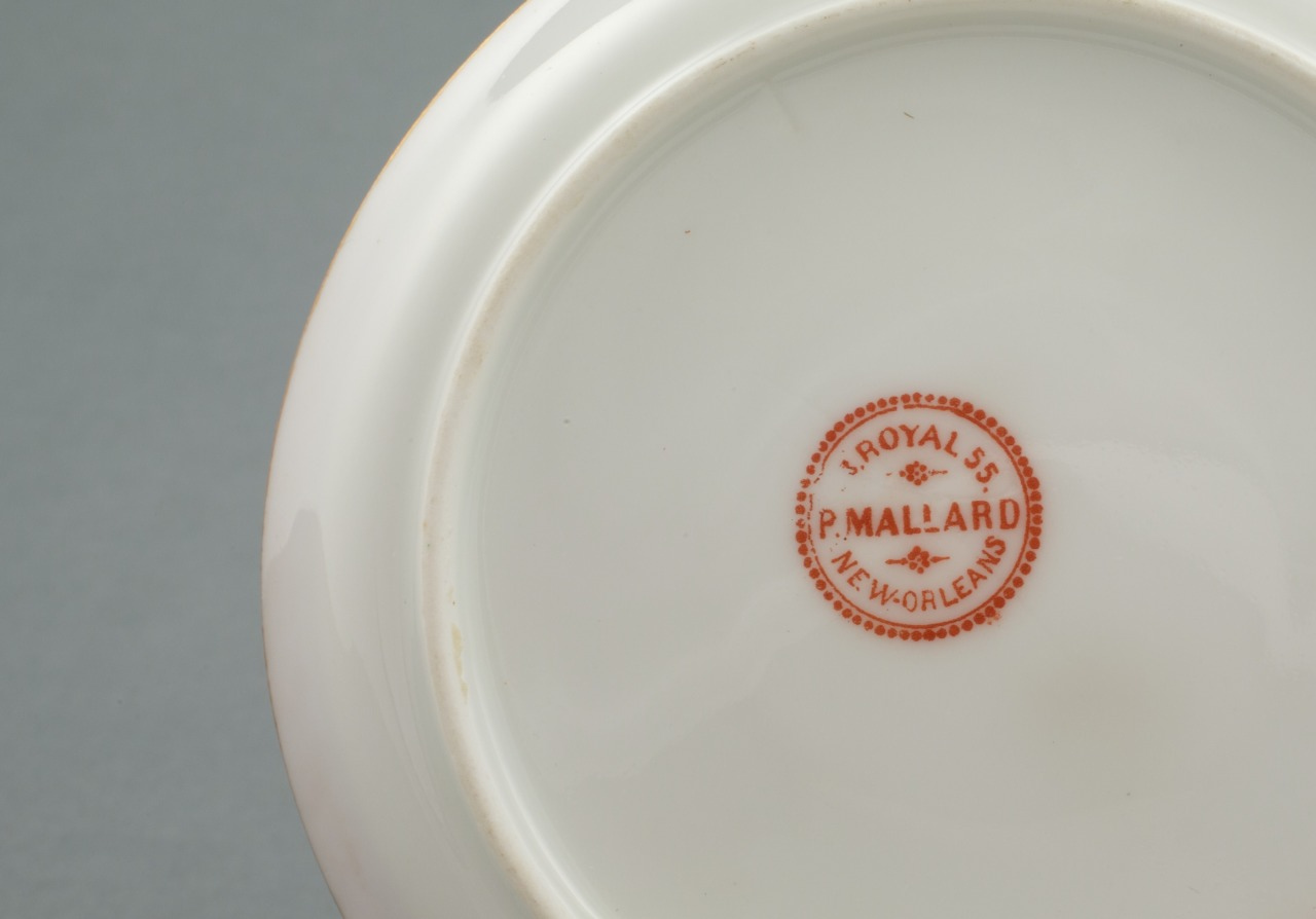 The image shows the underside of a white ceramic plate with a circular red hallmark reading J. Royal S. P. Mallard, New Orleans on a gray background.