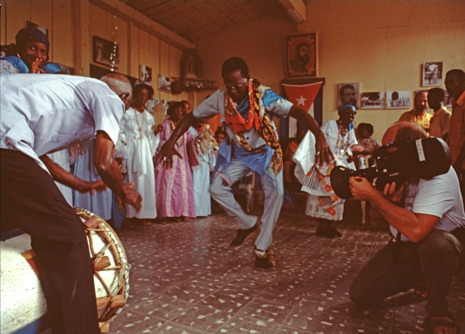 View of a Cuban folk dance where a man dances among women wearing floor length dresses and holding tamborines.