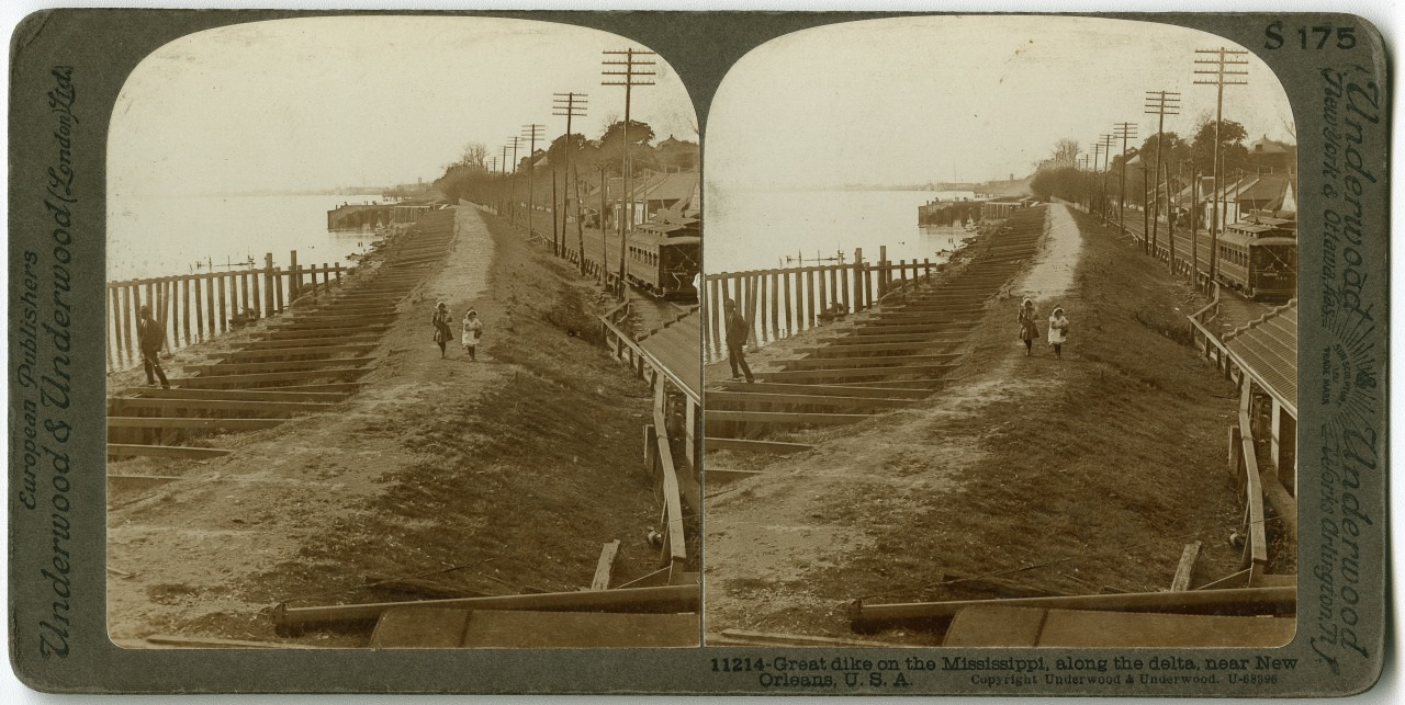 A sepia-toned stereoscopic image showing a levee along the Mississippi River near New Orleans. Two people walk on the levee, with wooden structures and utility poles lining the riverbank. Houses and trees are visible in the background.