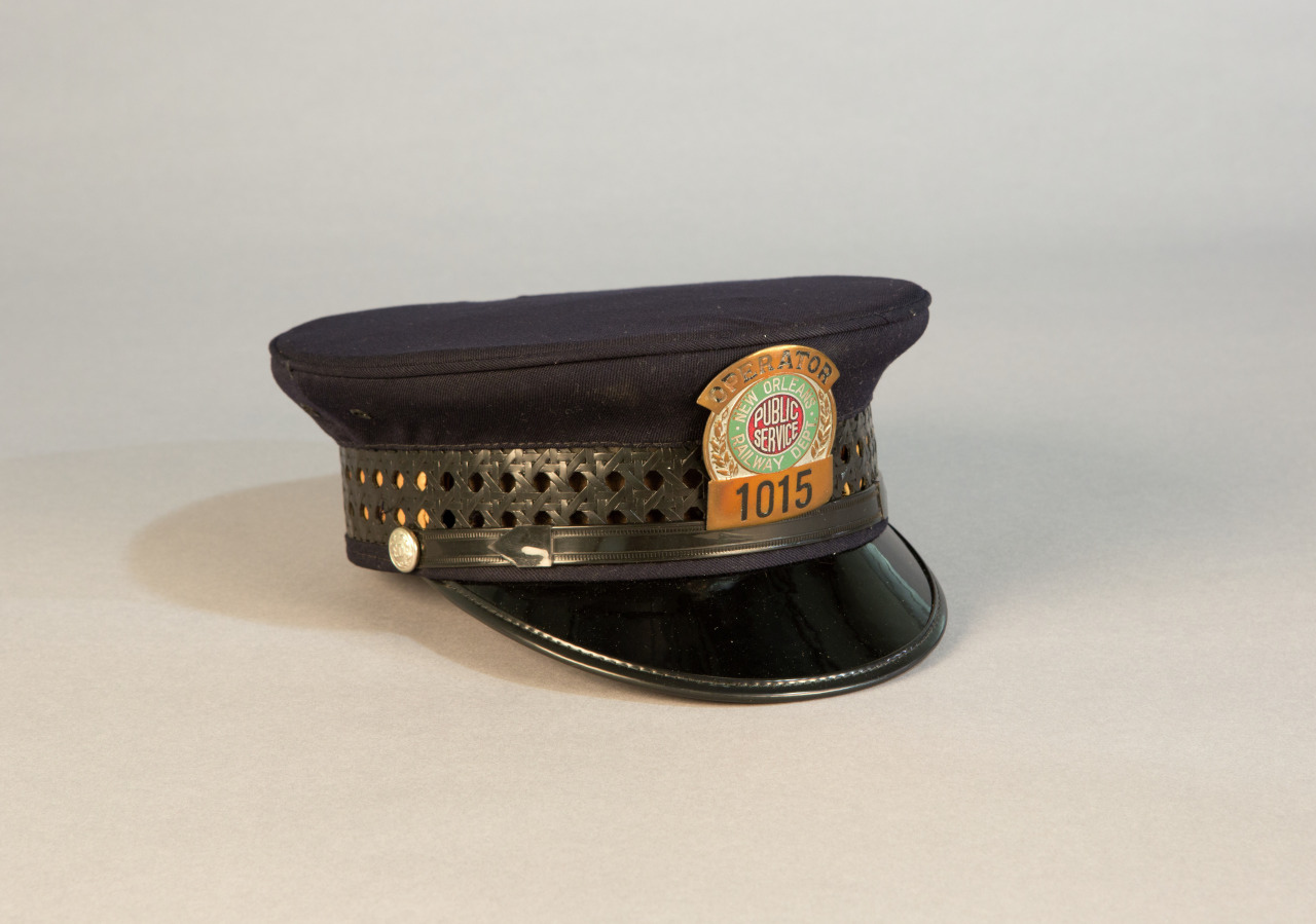 A black conductors hat with a glossy visor and metallic band. It features a round badge with RAPID TRANSIT and BIG FOUR on the front, along with the number 1015 on a rectangular plaque below. The background is a neutral gray.