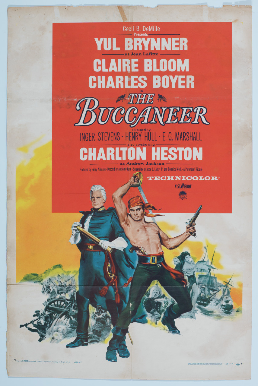 Vintage movie poster for The Buccaneer featuring a pirate with a red bandana holding a pistol and sword. Another man stands behind with a saber. Bold text includes cast names like Yul Brynner and Charlton Heston, and mentions Technicolor.
