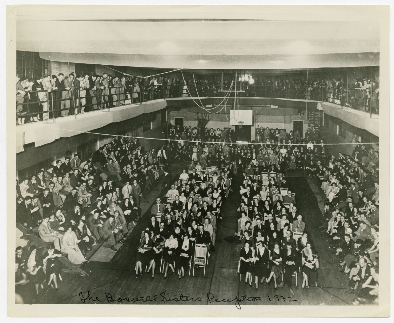 A large crowd seated and standing in a spacious, indoor venue during the The Bowral Sisters Reception 1932. People are gathered in rows with additional seating on the upper balconies. The atmosphere appears formal and celebratory.