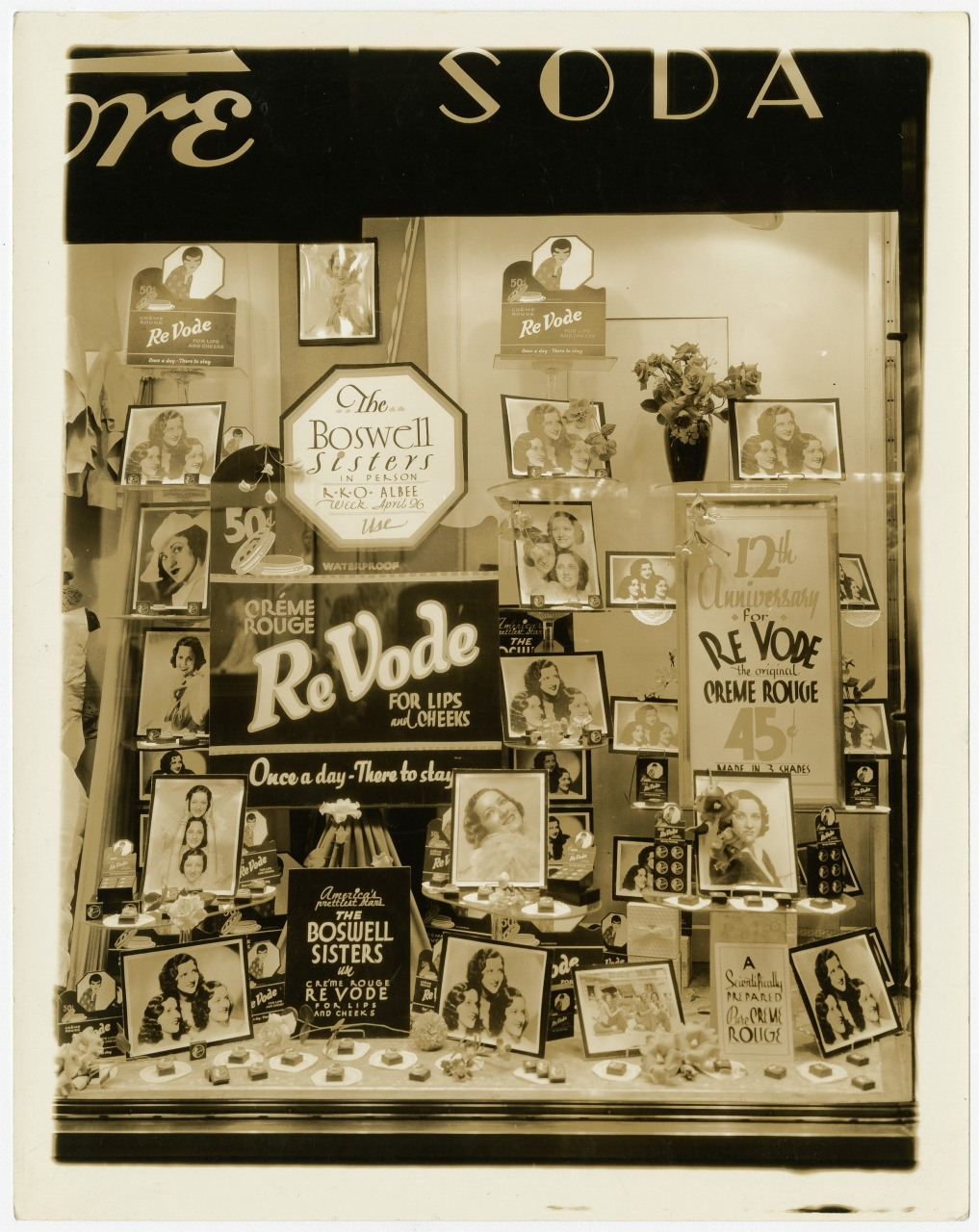 A vintage store window display featuring various posters and products promoting ReVode cream and rouge cosmetics, with images of the Boswell Sisters. Signs highlight promotions like Once a day—there to stay.