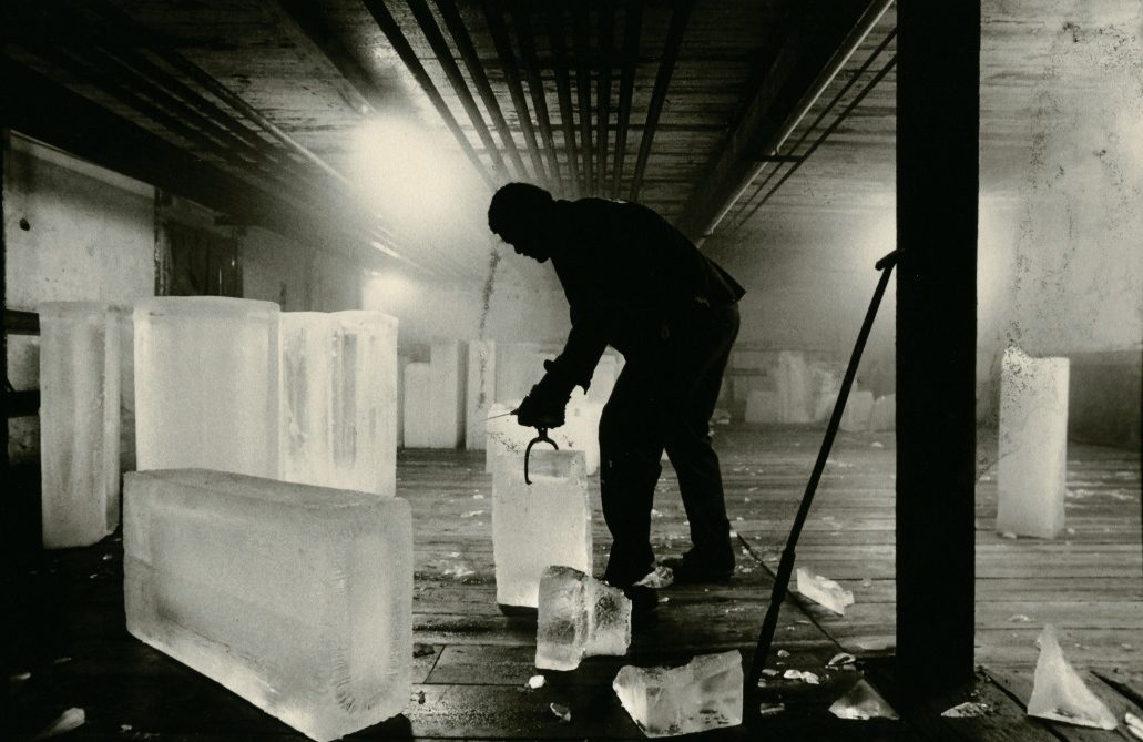 A worker in an ice factory grips an ice block with tongs.