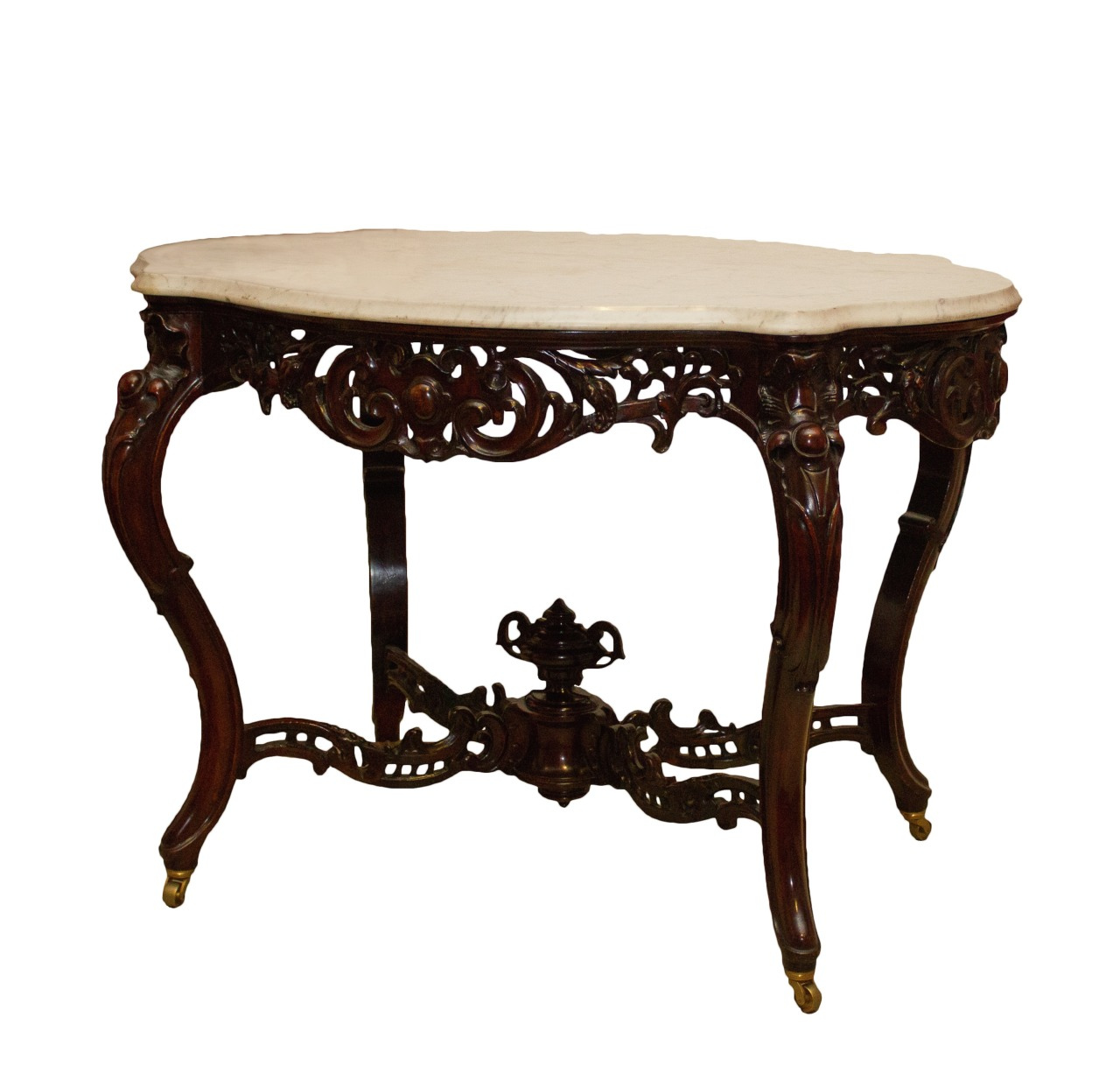 An ornate, vintage wooden table with intricate carvings and a white marble top. The table stands on four curved legs connected by a decorative crossbeam, showcasing elaborate floral and scroll designs.