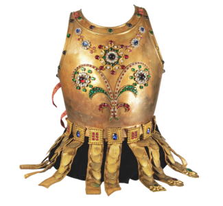A decorative golden breastplate adorned with colorful jewels and intricate designs, featuring a floral pattern at the center. The bottom edge has a series of gold fringe-like extensions.