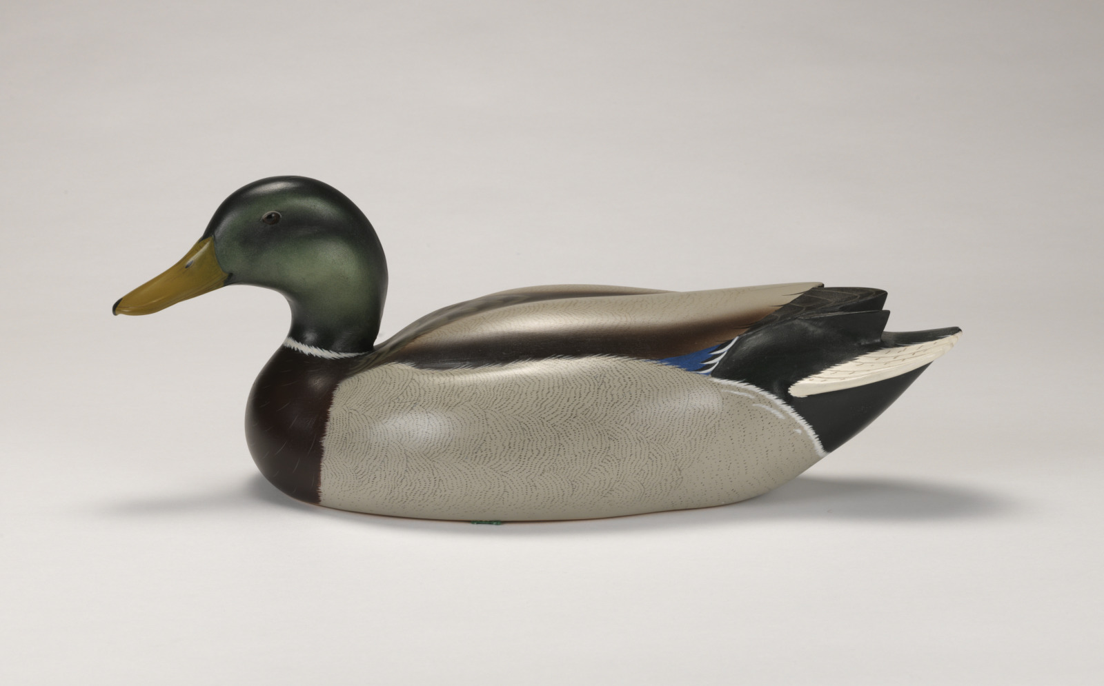 Realistic carving of a mallard duck depicted as if floating on water.