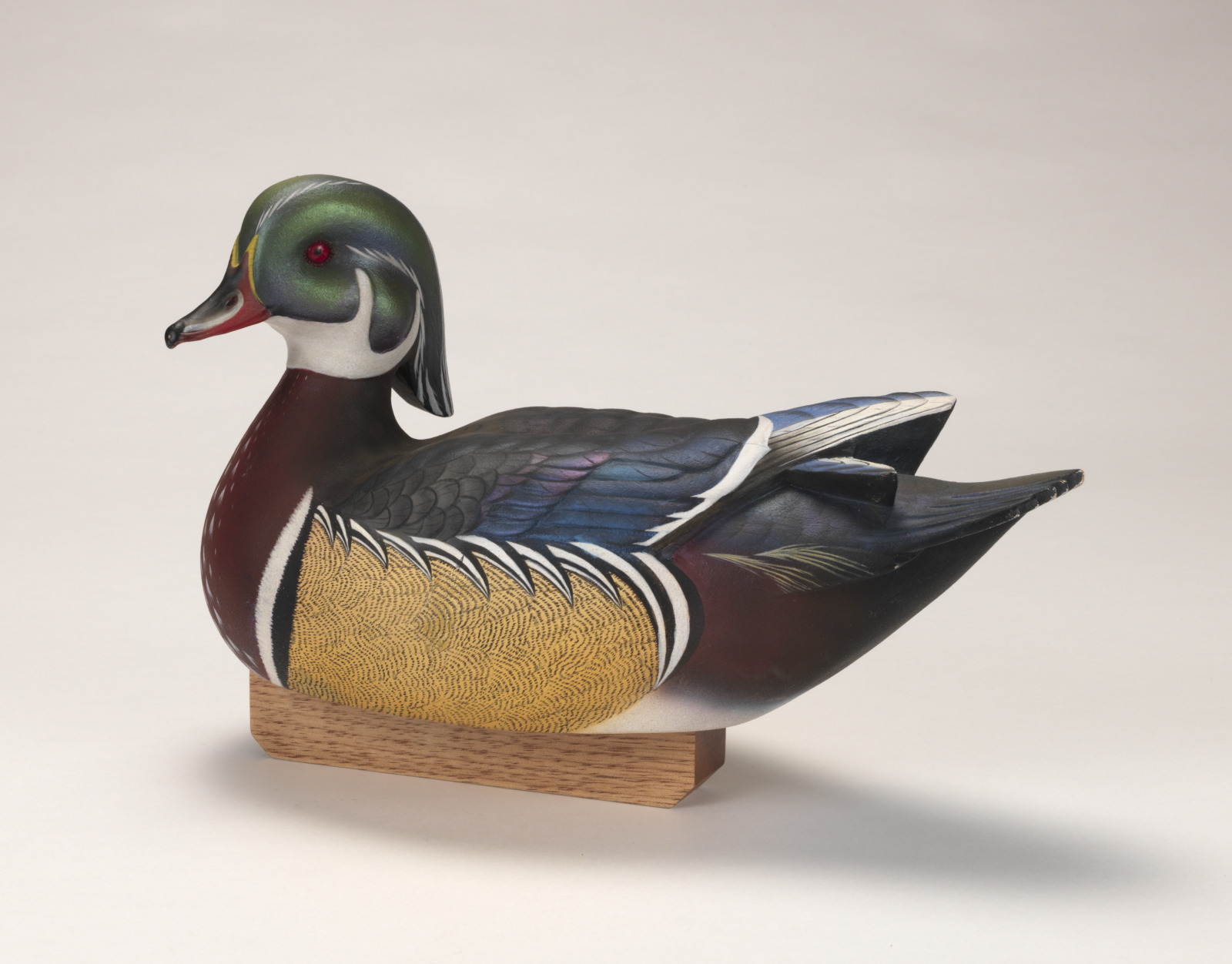 A realistic carving of a wood duck depicted as if floating on water, attached to a wooden base.