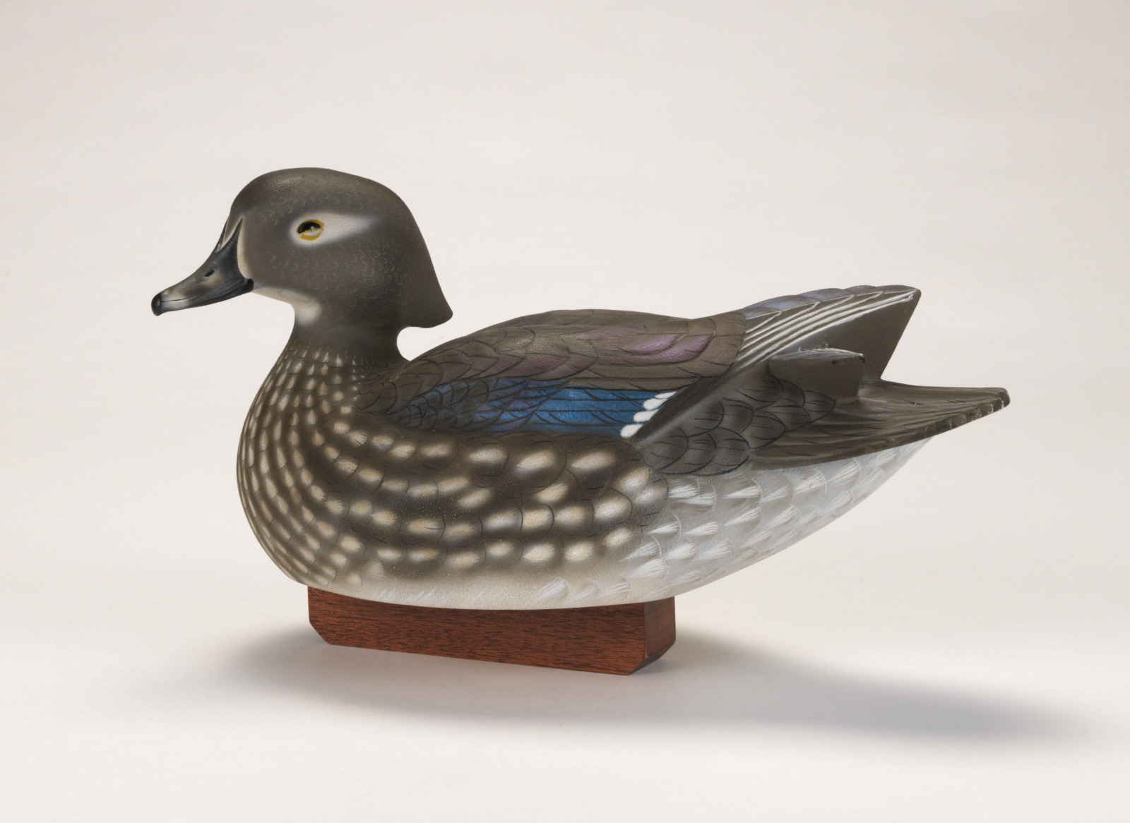 A realistic carving of a wood duck depicted as if floating on water, attached to a wood base.