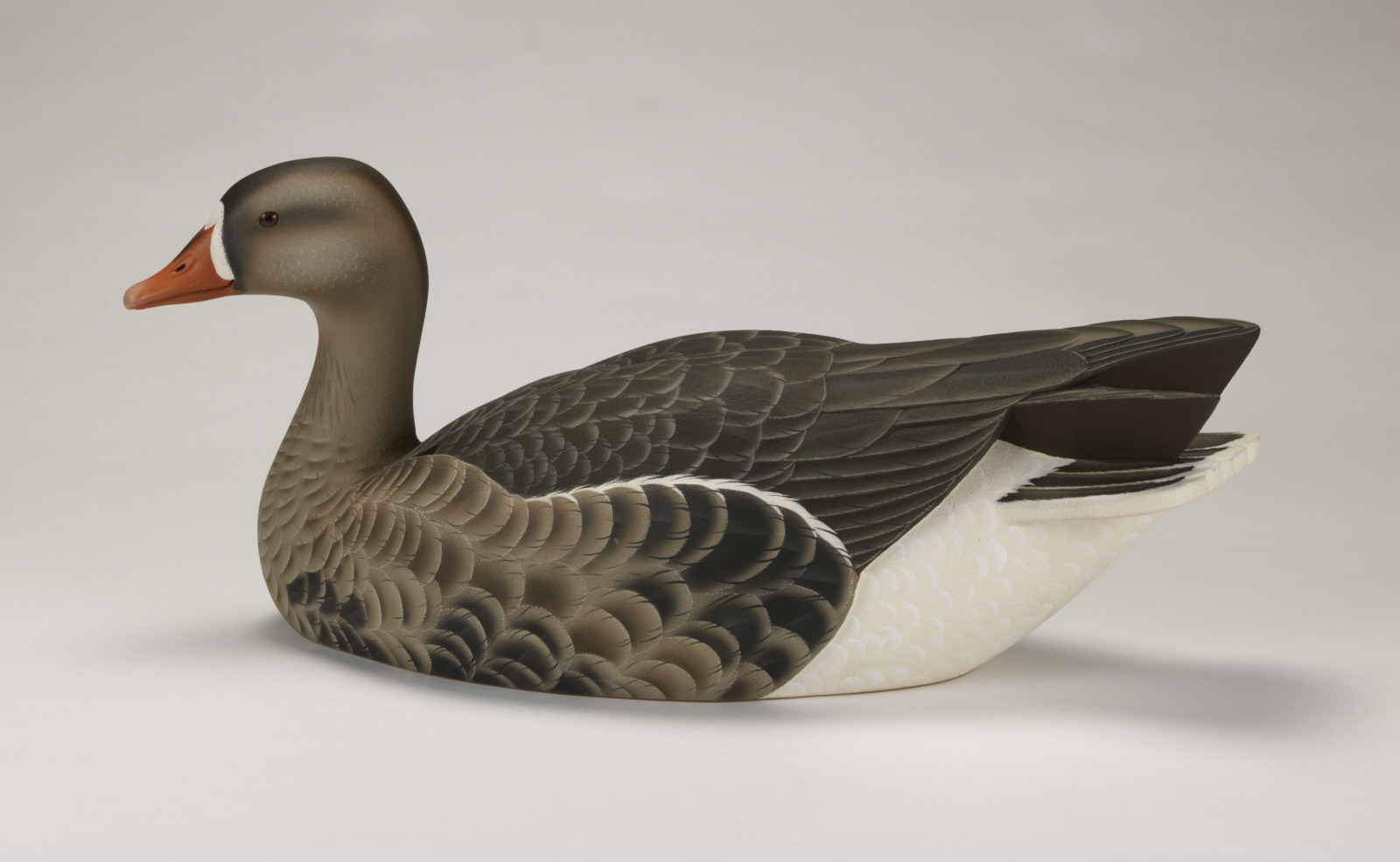 A realistic carving of a white fronted goose, depicted as if floating on water.