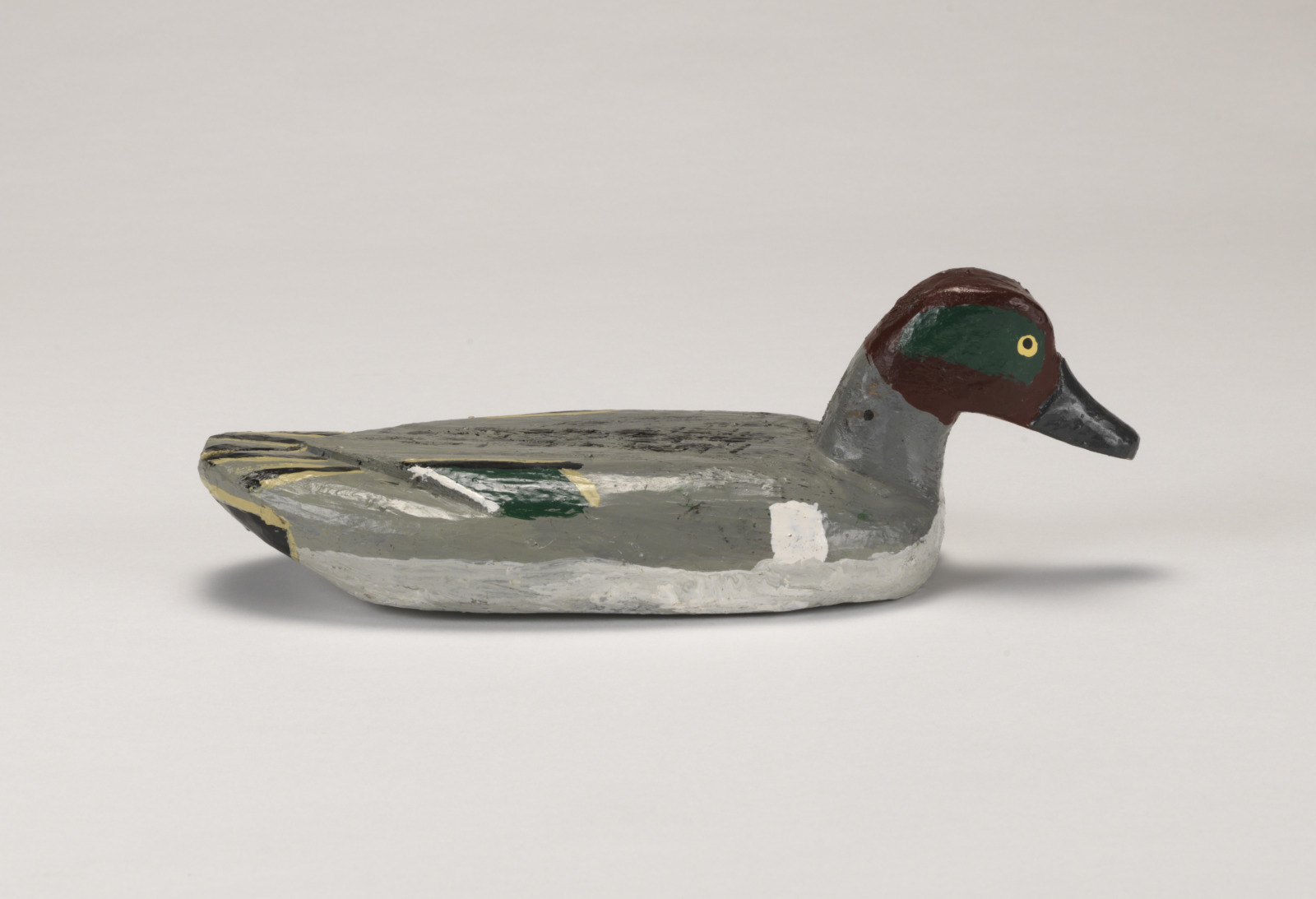 A realistic carving of a green wing teal duck depicted as if floating on water.