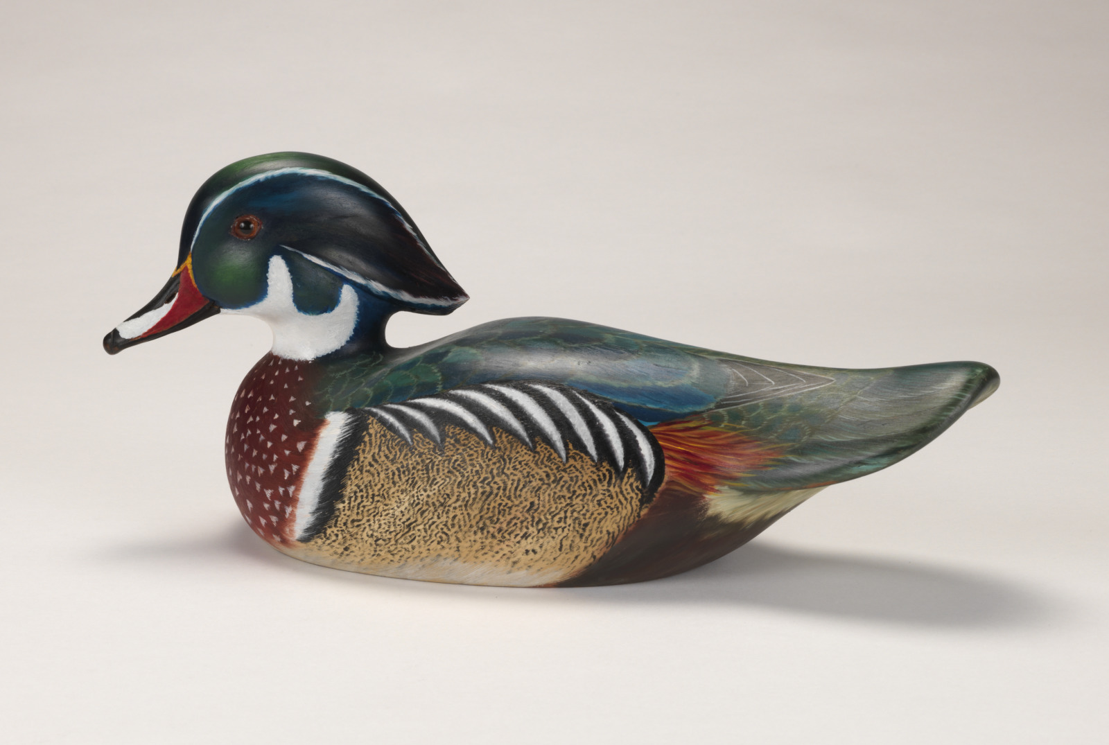 A realistic carving of a wood duck (drake) depicted as if floating on water.