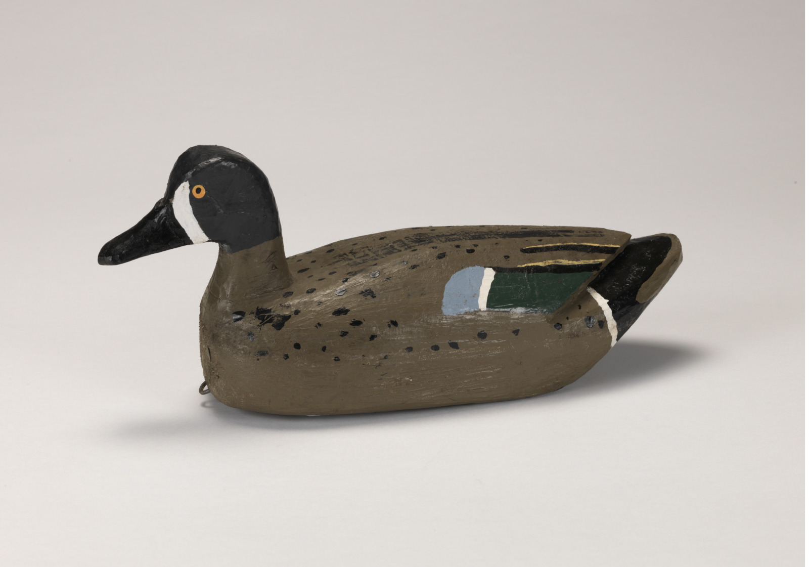 A realistic carving of a blue wing teal duck depicted as if floating on water.