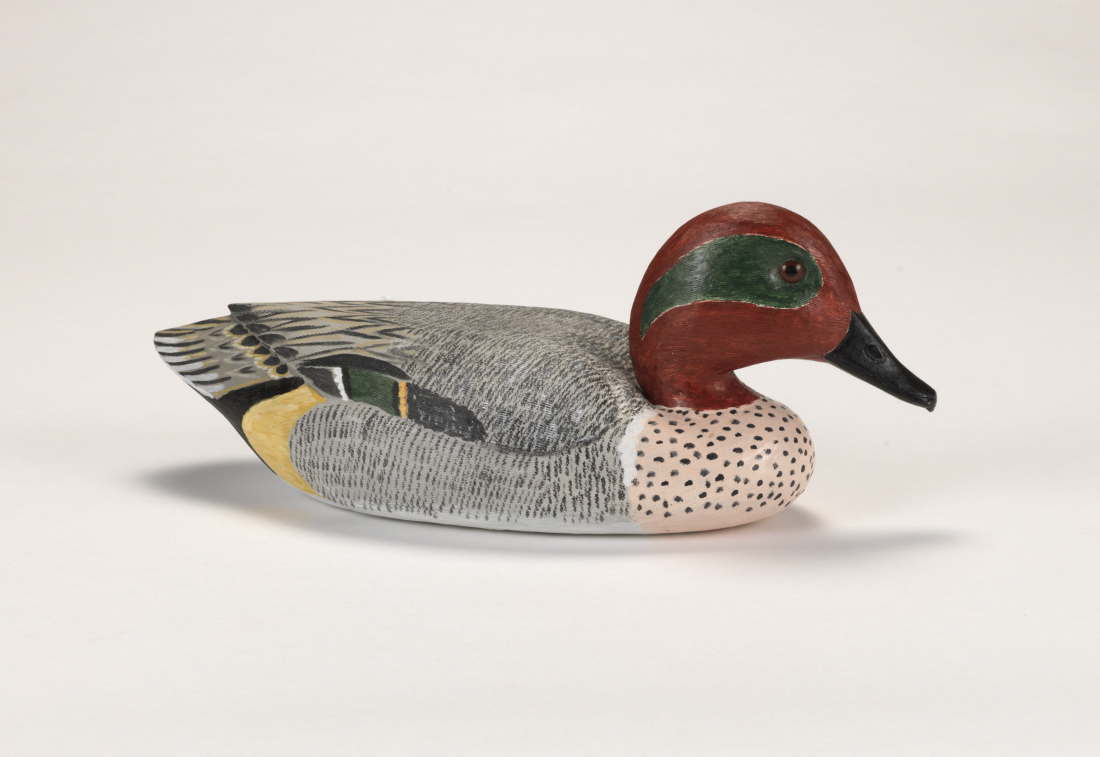 A realistic carving of a green wing teal duck, depicted as if floating on water.
