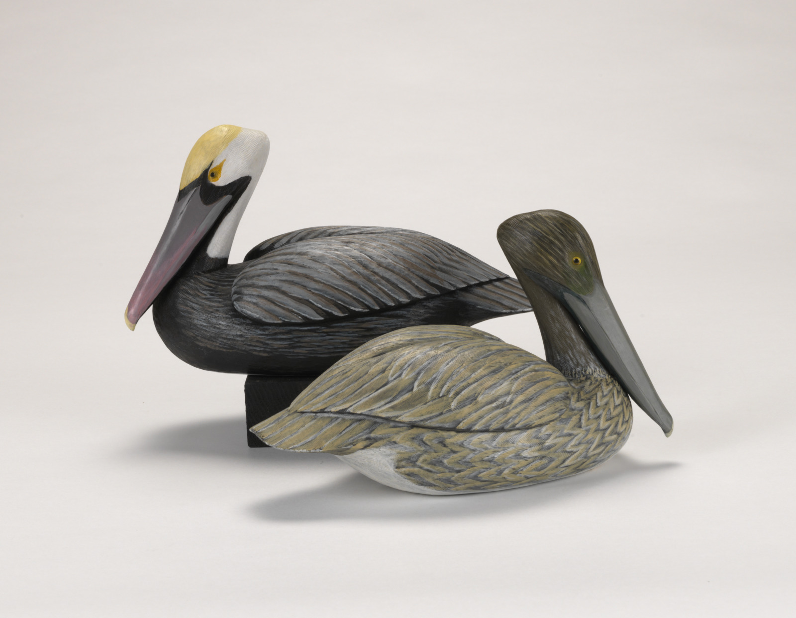 Two realistically carved brown pelicans, facing opposite directions from eachother.