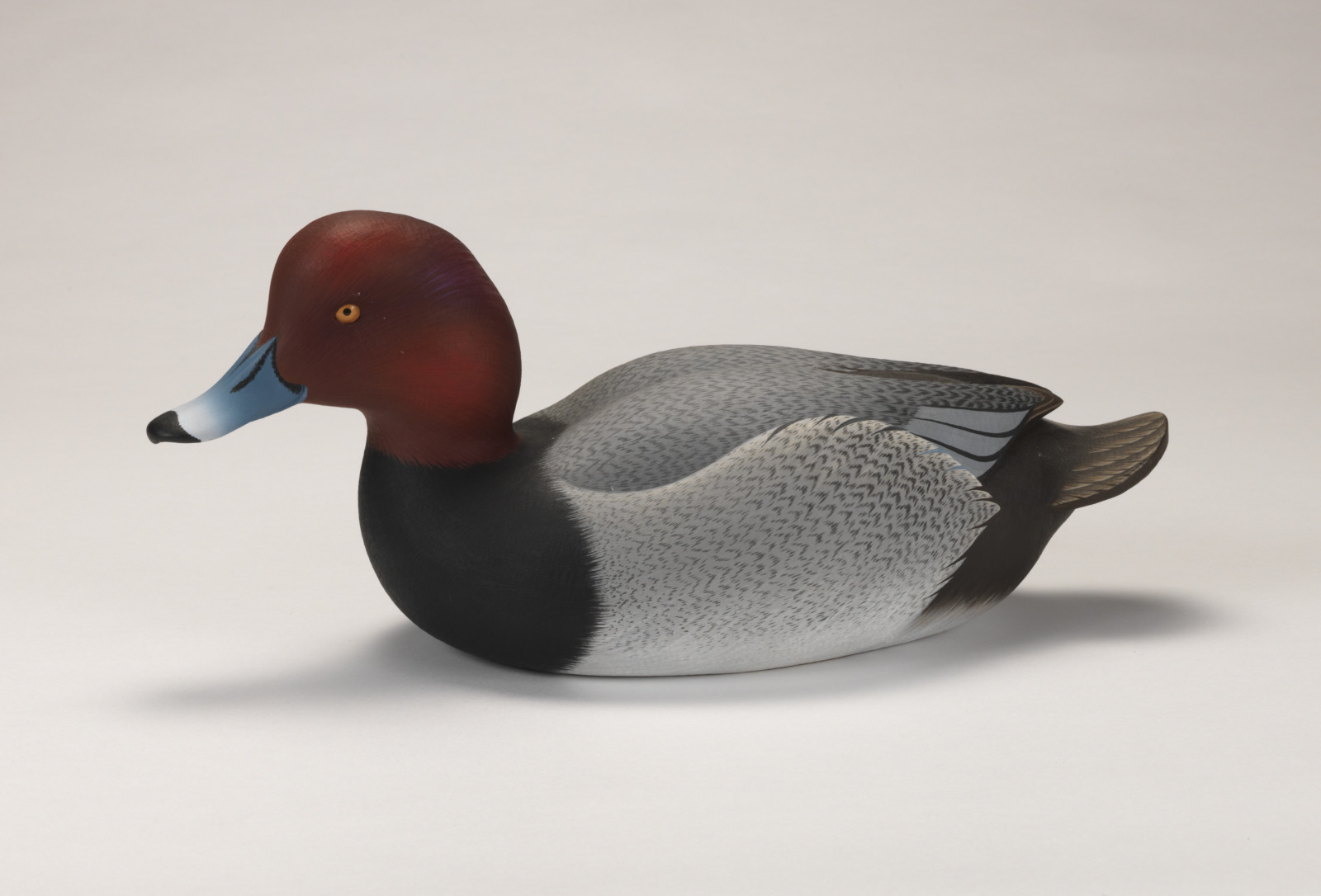 A realistic carving of a redhead duck depicted as if floating on water.