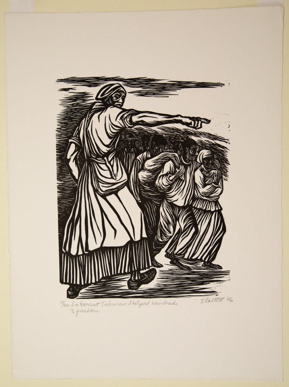 A black and white illustration depicts a woman in traditional clothing pointing with her right hand. Behind her, three individuals appear to be walking, carrying bundles on their heads. The style is reminiscent of a woodcut print.