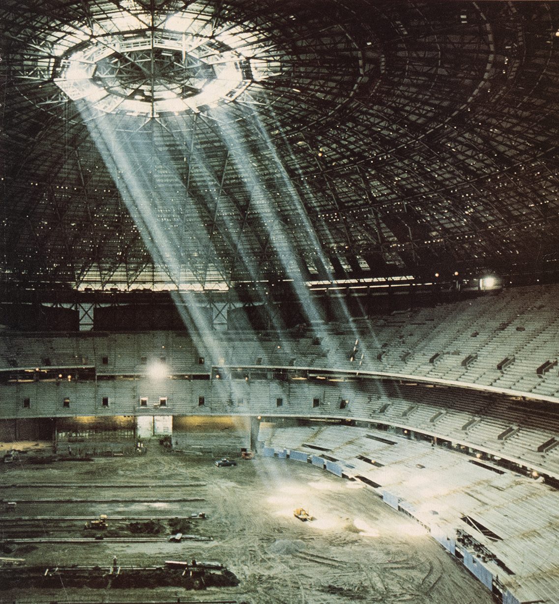 A photo of the Superdome under construction shows a shaft of light shining through a hole at the top of the Dome onto the field below.