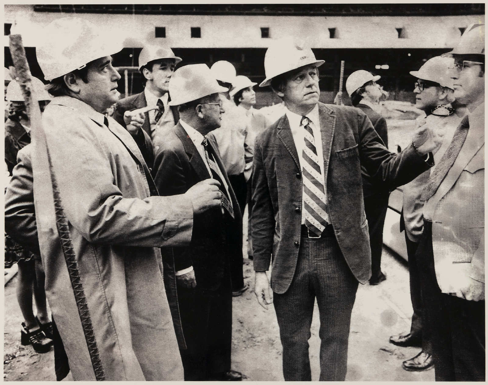 A group of men wearing business suits and hard hats tour the construction site of the Super Dome.