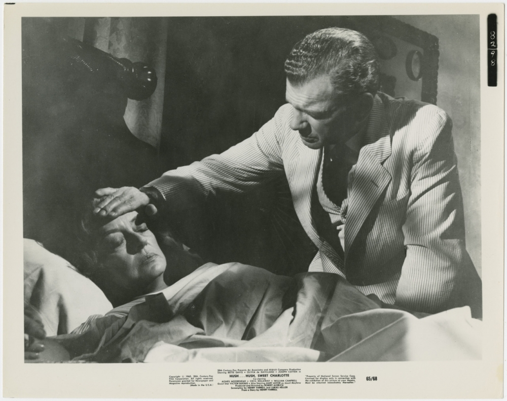 A black-and-white image of a man in a striped suit gently touching the forehead of a woman who is lying in bed, possibly unwell. The scene appears intimate and caring, with a vintage atmosphere.