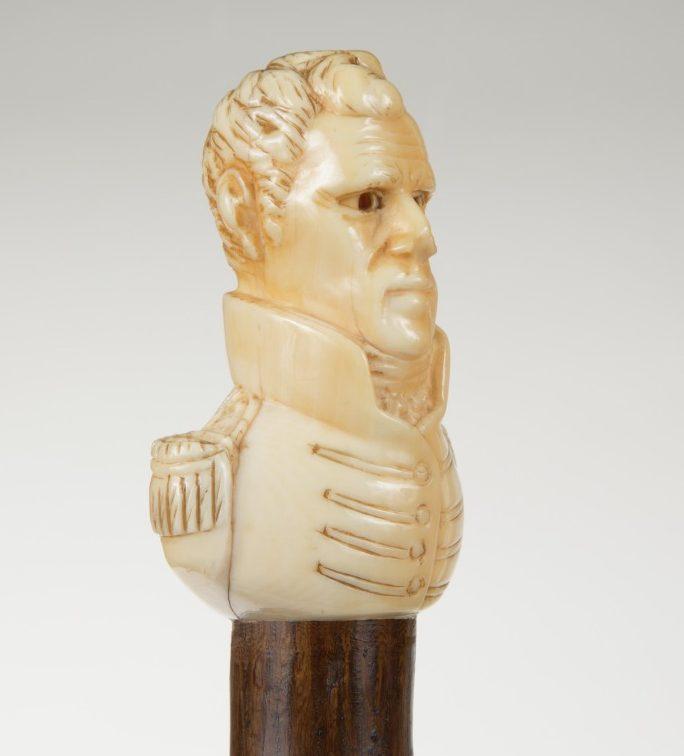 Ivory carving of a mans bust with detailed features, including a high-collared military-style jacket. The sculpture is mounted on a wooden base.