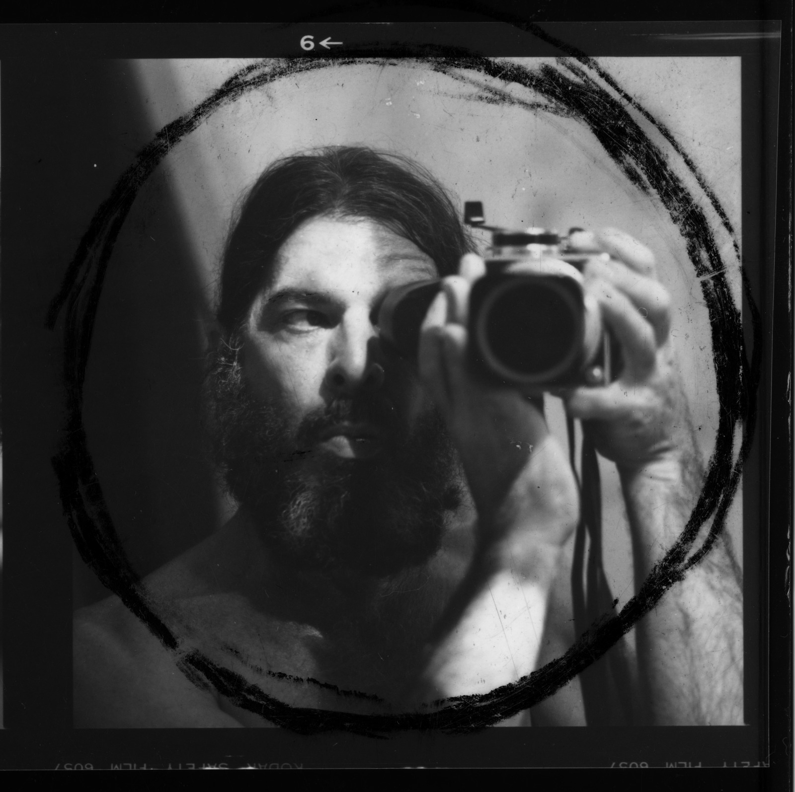 A black and white self portrait by George Dureau. Photo shows the artist pointing his camera at a mirror. A black circle surrounds the subject.