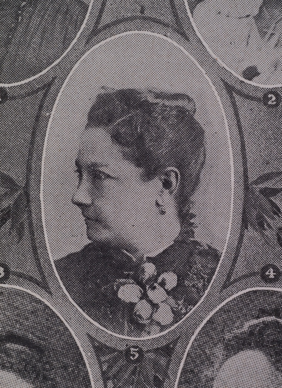 A vintage black and white photograph of a woman in a formal pose, her hair styled in an updo. The image is oval-shaped and surrounded by decorative elements. She is looking to the left and wears a dark outfit with a floral brooch.