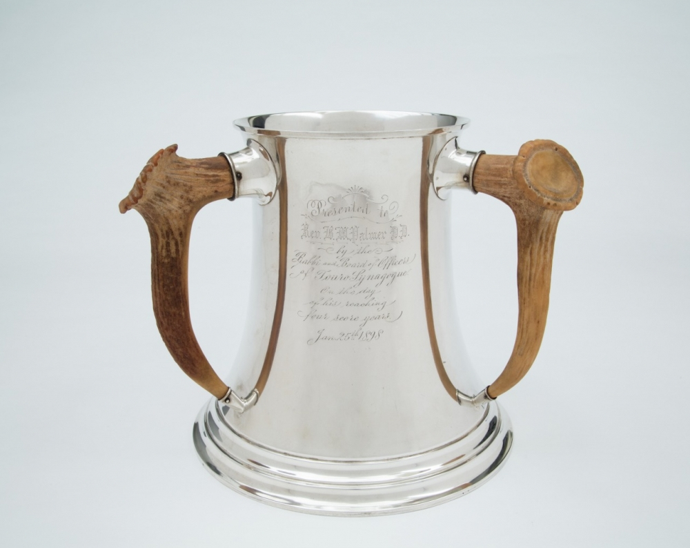 A silver trophy with two antler handles, engraved with intricate text, displayed against a plain background.