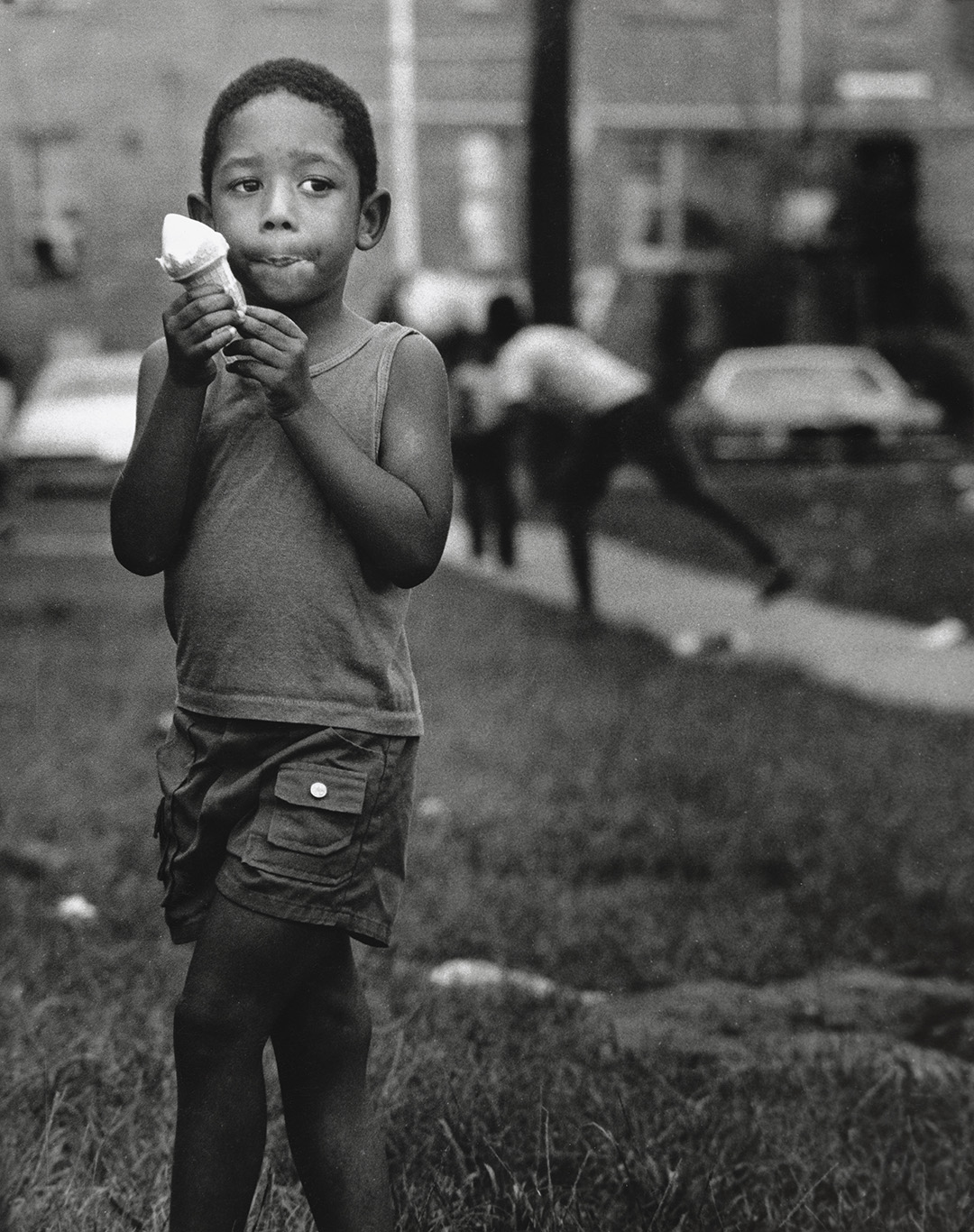 Black and white of a child eating an ice cream cone outside of a building.