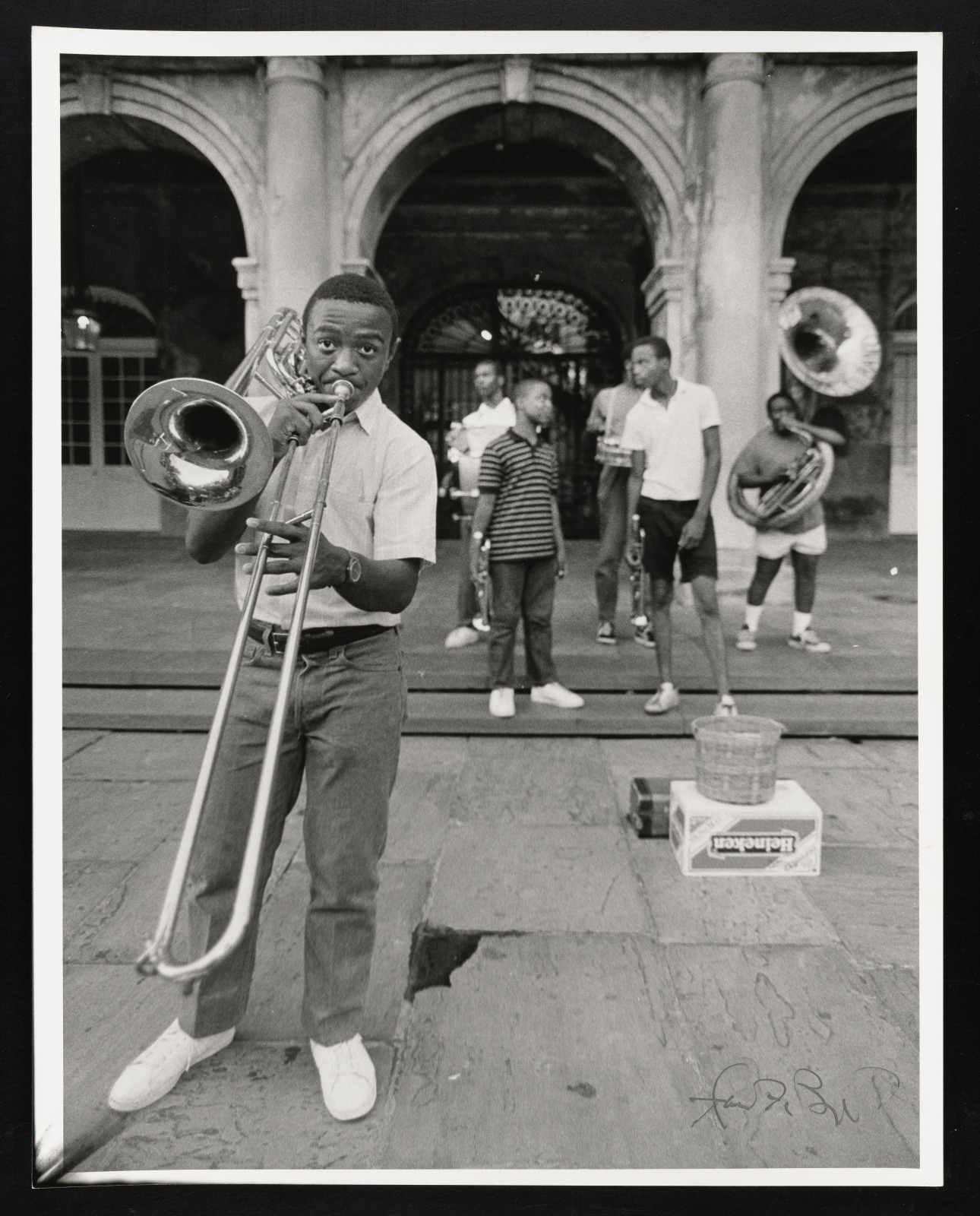 A black and white photo of young men playing brass instruments (trombones, trumpets, and tubas) in Jackson Square, New Orleans.