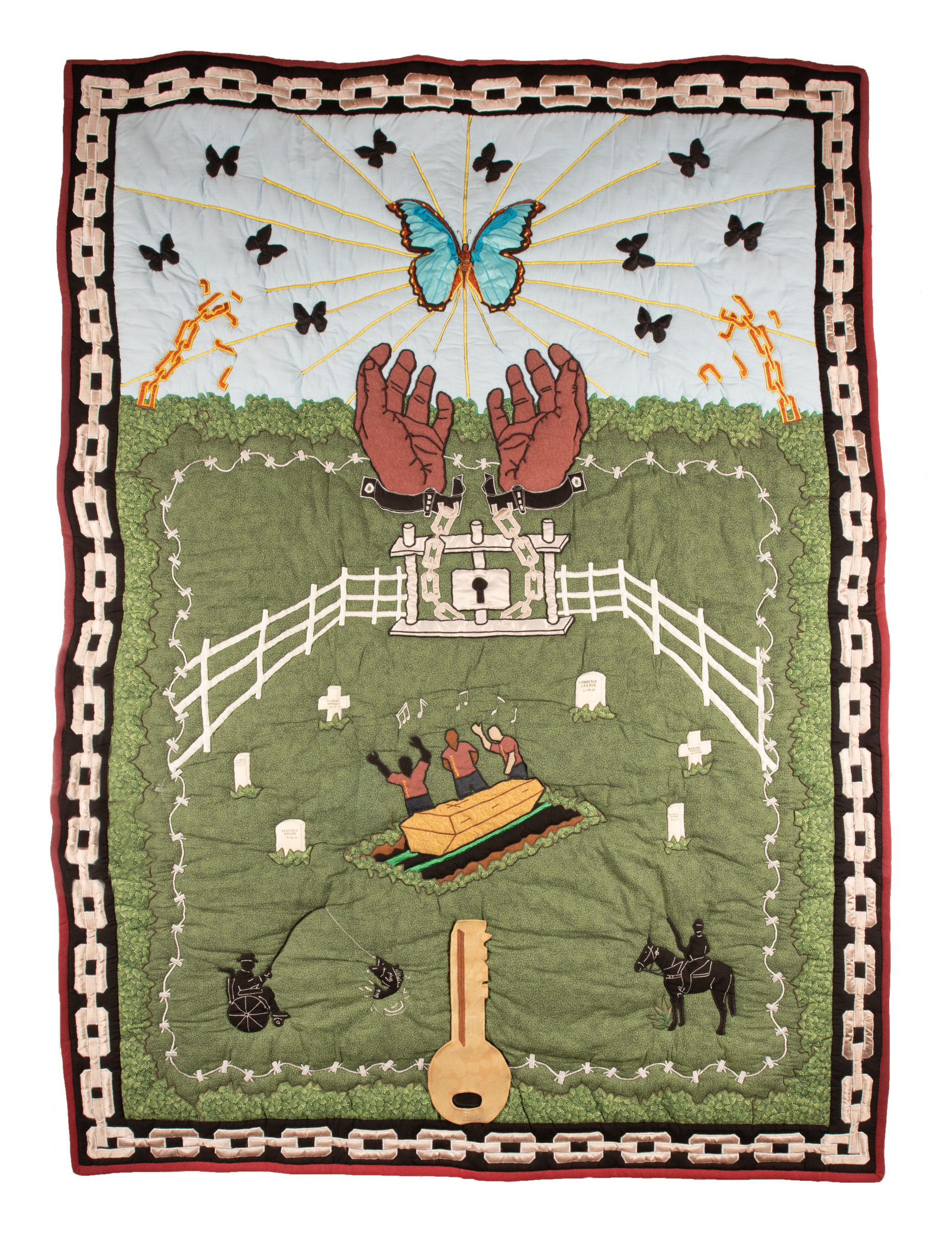 A vibrant quilt depicts large hands releasing butterflies, a central butterfly surrounded by rays, people at a gravesite, a white fence, two horses, and a large key symbol at the bottom, all framed by a chain design on a green background.