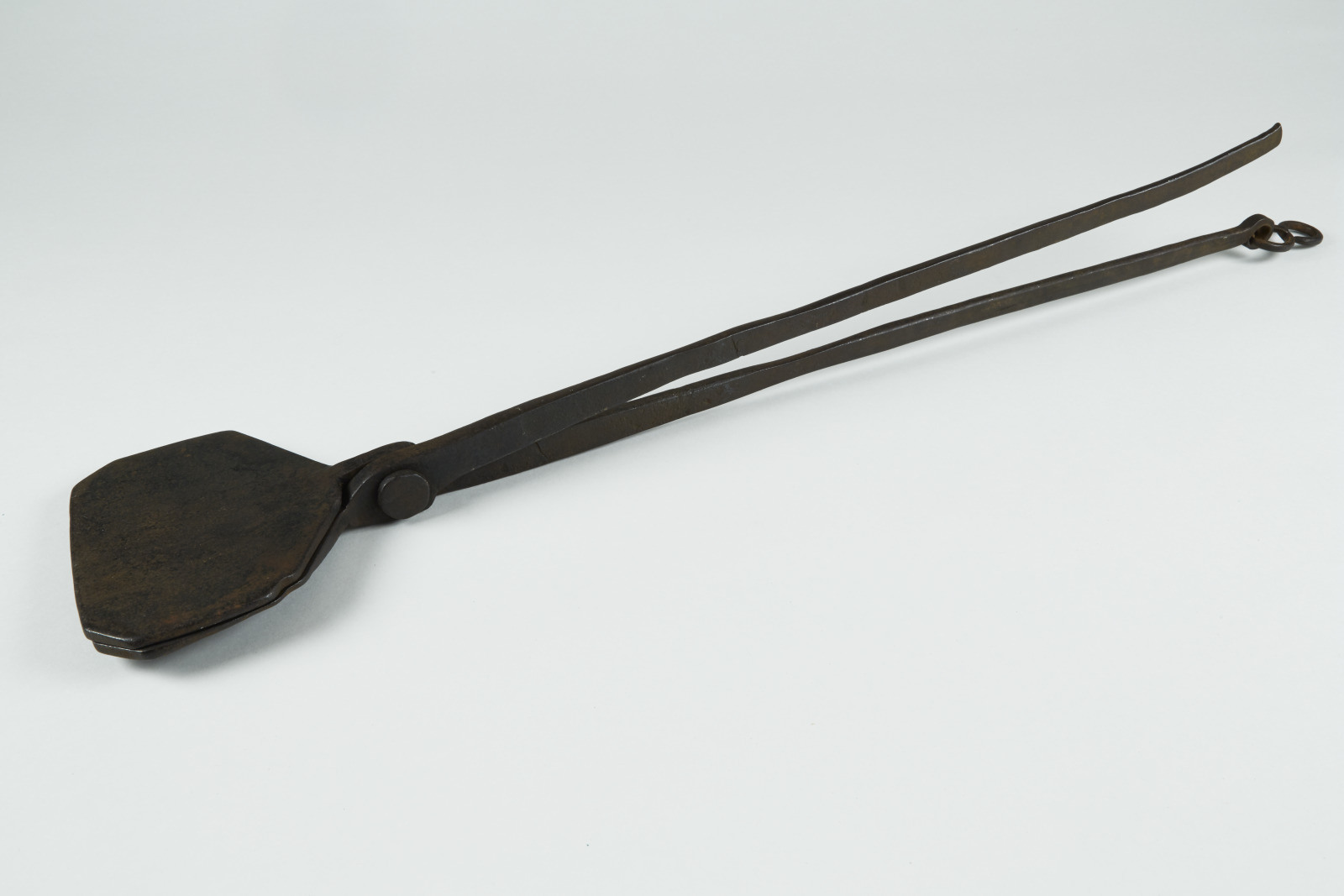 A vintage, rusty pair of blacksmith tongs with elongated handles and flat, wide jaws against a plain white background.