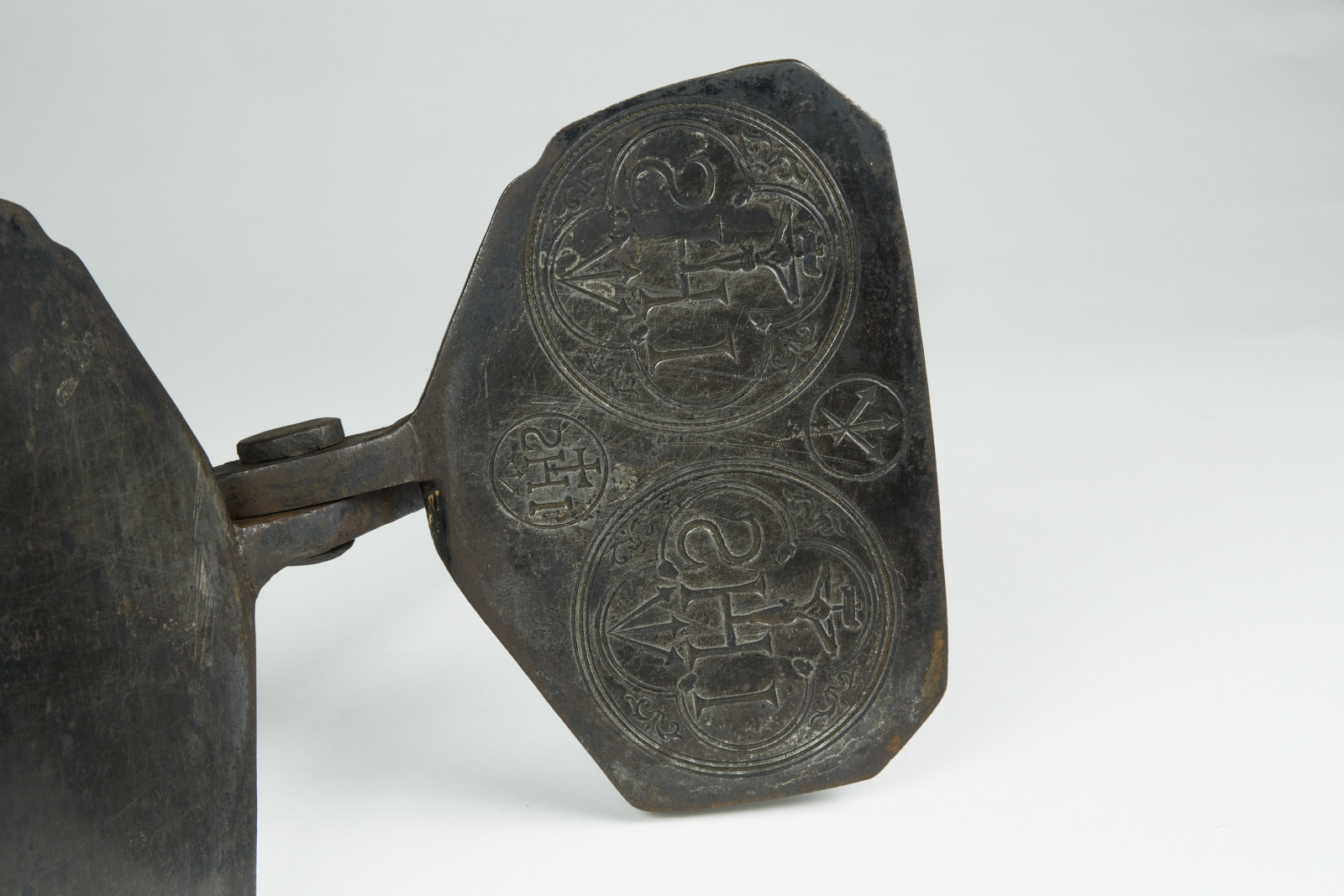 A close-up of an ancient artifact showcasing intricate circular engravings with faded symbols and a star design. The piece is metallic with a worn, darkened surface, suggesting historical significance.